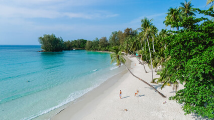 Soft white sands meet crystal-clear waters on Koh Kood Island, Thailand. Visitors indulge in sunbathing and leisure activities surrounded by lush palm trees and a tranquil atmosphere
