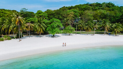 Couple strolls hand in hand along the white sandy beach of Koh Kham Thailand surrounded by lush...
