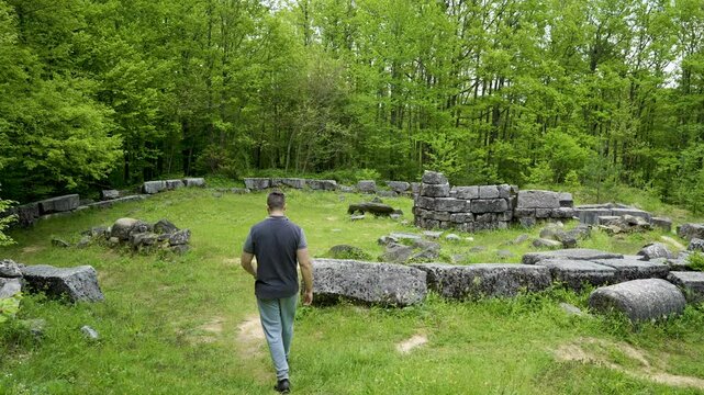 Walking towards the ruins of Mishkova Niva tomb, a tourist looks around to the trees and the ancient structures located in Srandzha Mountain in the municipality of Malko Tarnovo in Bulgaria.