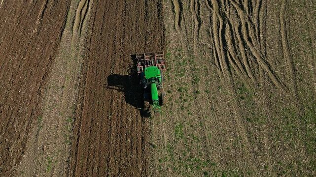 Following drone movement from a green tractor making parallel plowing in the plowed field.