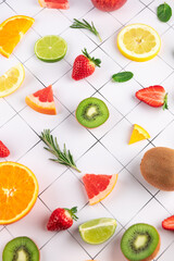 Creative arrangement of assorted fruits on white geometric background. Orange, lemon, lime and grapefruit slices next to strawberries and kiwi. Concept of summer and natural nutrition