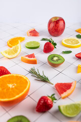 Various fruits in an artistic arrangement on white surface with grid. Kiwi, strawberries, lemon,...