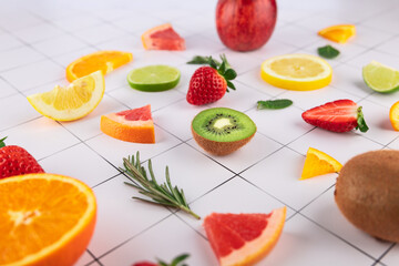 Creative composition of fresh fruits on white tile background. Kiwi in foreground, surrounded by strawberries, citrus fruits and aromatic herbs. Vibrant colors. Healthy eating concept