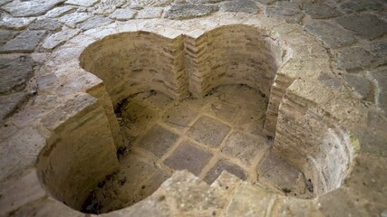 A cross-shaped baptismal font is carved into the stone floor of a medieval structure in Pliska, Bulgaria, once the religious center of the First Bulgarian Empire.