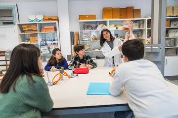 Smiling science teacher showing anatomical model to attentive elementary school students during a biology class