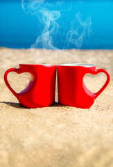 two heart shaped mugs with tea on the seash
