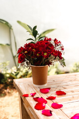 A small glass with a bouquet of flowers on a wooden table and rose petals
