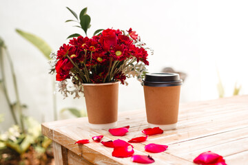 Hot coffee to take away next to a small bouquet in a paper cup