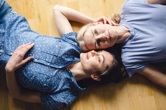 Mother and daughter lying on a wooden floor at home, showcasing trust and care