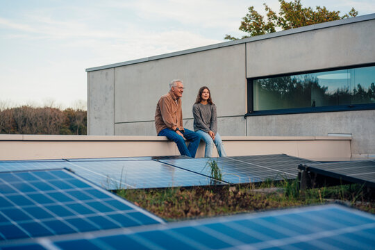 Grandfather and granddaughter sitting on a rooftop with solar panels discussing sustainable energy