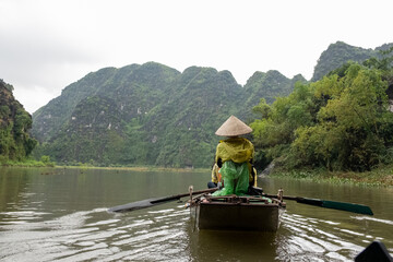 A boat rower in a green jacket paddles calmly through the river in Ninh Bình, Vietnam on December 26, 2019 © Larry Zhou