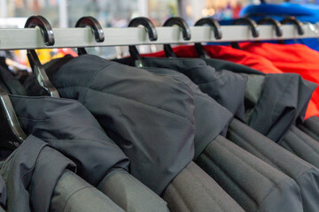 Many outdoor jackets on hangers in a clothing store, close-up, selective focus