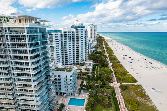 Miami Beach, Florida &ndash; Aerial photo shows modern beachfront condos with pools, green spaces, and a busy oceanfront boardwalk.