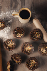 Freshly baked brown muffins on baking paper, coffee mug, flour on a table, top view, vertical image.