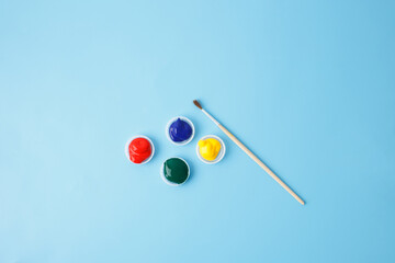 Four colorful paint containers and a fine-tip brush for art projects, creative hobbies, and educational activities, ideal for businesses promoting art supplies or DIY creativity,