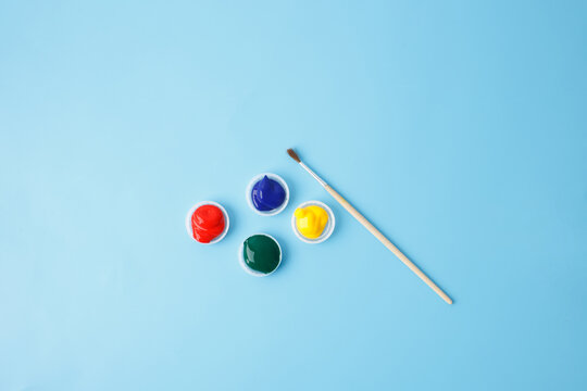 Four colorful paint containers and a fine-tip brush for art projects, creative hobbies, and educational activities, ideal for businesses promoting art supplies or DIY creativity, - Powered by Adobe