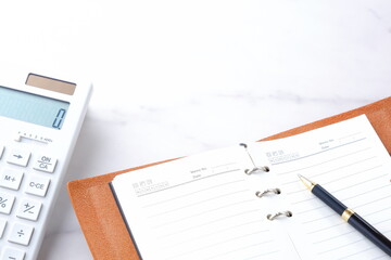 電卓と手帳でデスクワークをしているイメージ
