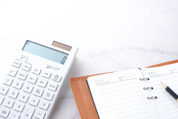 電卓と手帳でデスクワークをしているイメージ
