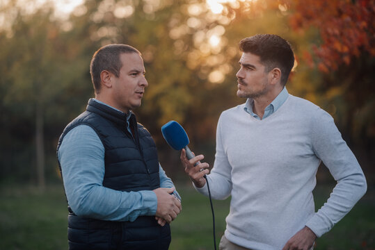 Journalist interviewing man outdoors in a park during sunset