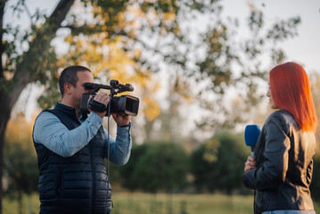 Cameraman filming female reporter holding microphone in park © Ljustina