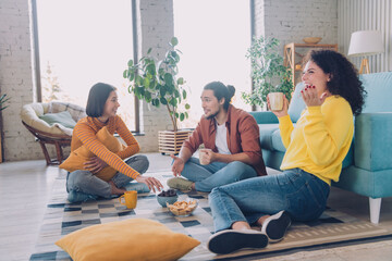 Young friends enjoying leisure time together inside a cozy living room, sharing snacks and warm beverages