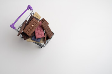 Multicolored chocolate bars in a shopping cart on a light background. Healthy eating concept, delicious chocolates, diet, sugar
