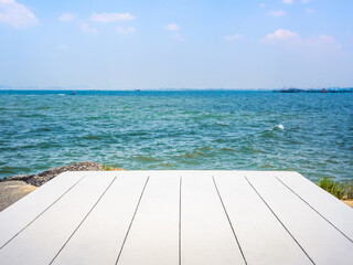 Fototapeta premium Summer vacation concept with seascape background for placed products. Empty white wood plank top table on tropical sea ocean scene on open blue sky and white clouds, horizontal abstract background.