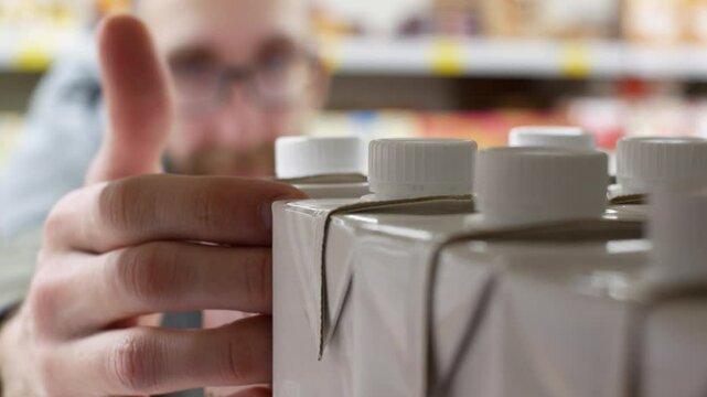 Close-up of many white cartons of milk on a supermarket shelf and male consumer takes one