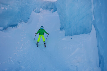 Skier in bright gear navigates icy glacier passage at mountains