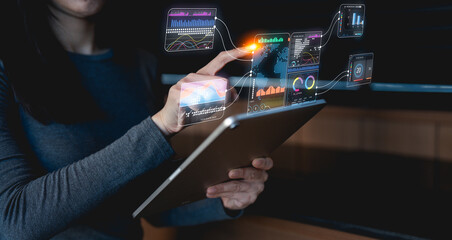 A person interacts with a digital tablet displaying various data visualizations and analytics in a...