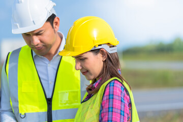 A team of professionals in the renewable energy industry are analyzing business data on-site, led by a female engineer and a male engineer reviewing project details together.