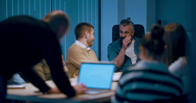 A diverse team of young professionals collaborates in a modern office conference room. Businesspeople discuss strategy, technology, and planning, using laptops to develop an innovative e-commerce