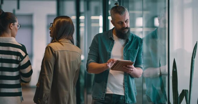 Bearded senior multiracial businessman smiling and looking at the camera. Mature CEO holding a digital tablet in a modern open space startup coworking office showcasing leadership in smart casual - Powered by Adobe