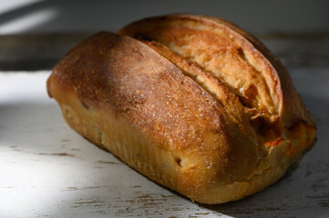 Freshly baked loaf of artisanal bread resting on rustic wooden table with soft natural light illuminating its crusty surface