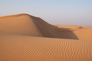 Desert scene captures the beauty of natural sand dunes with intricate patterns and late afternoon shadows. The vast landscape highlights the serenity and endlessness of the desert.