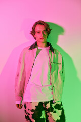 Young man showcases trendy fashion under vibrant pink and green lighting in urban backdrop