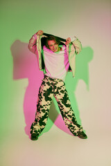 Fashionable young man showcases trendy outfit with confidence in vibrant studio lighting