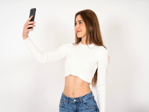 Caucasian young girl wearing white T-shirt smiling and taking a selfie ready to post it on her social media.