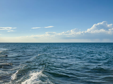 dynamic sea surface under a bright blue sky with clouds. straight horizon. open seascape. sea waterline. sea background. 