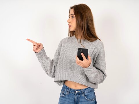 Stunned Caucasian young girl wearing grey sweater points sideways right copy space, recommends product, sees astonishing thing