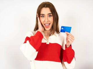 Astonished positive Caucasian young girl wearing striped sweater arm face hold bank plastic card impressed functions