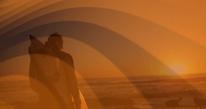 Carrying surfboard, surfer walking along beach during sunset with ocean view