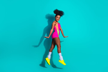 Young stylish woman in vibrant activewear posing energetically on a teal background, exuding...