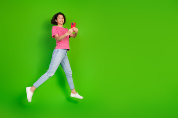 Young woman with curly hair in striped t-shirt using mobile phone, leaping joyfully against a...
