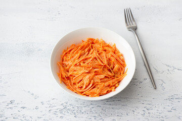 Carrot salad with sour cream and cinnamon in a white bowl on a light rustic background