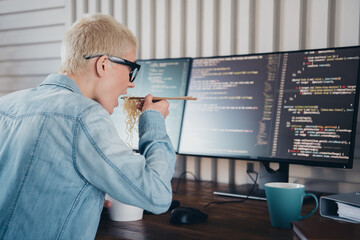 Young programmer working remotely in a casual setting, enjoying a quick meal while coding on a...