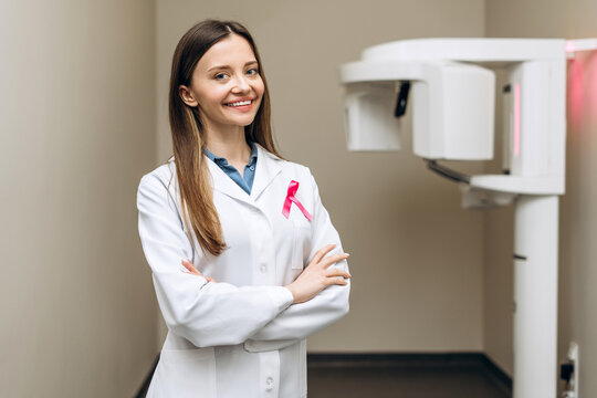 Smiling female oncologist with ribbon crossing arms, breast cancer month