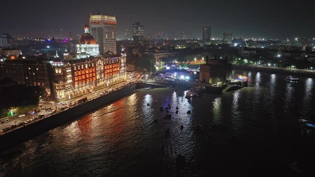 Aerial night view of the Gateway of India. Cityscape of old Mumbai town. Evening weather on the seashore of Mumbai. Cinematic view of the Taj Palace Hotel. Fishing boats sail in the sea in the evening