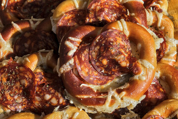 Close-up of pretzels topped with pepperoni slices and melted cheese, garnished with herbs, offering a visually appealing savory snack.