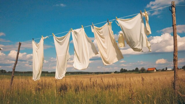 A clothesline with white sheets hanging in a rural setting, suggesting a laundry day during sunny weather.
